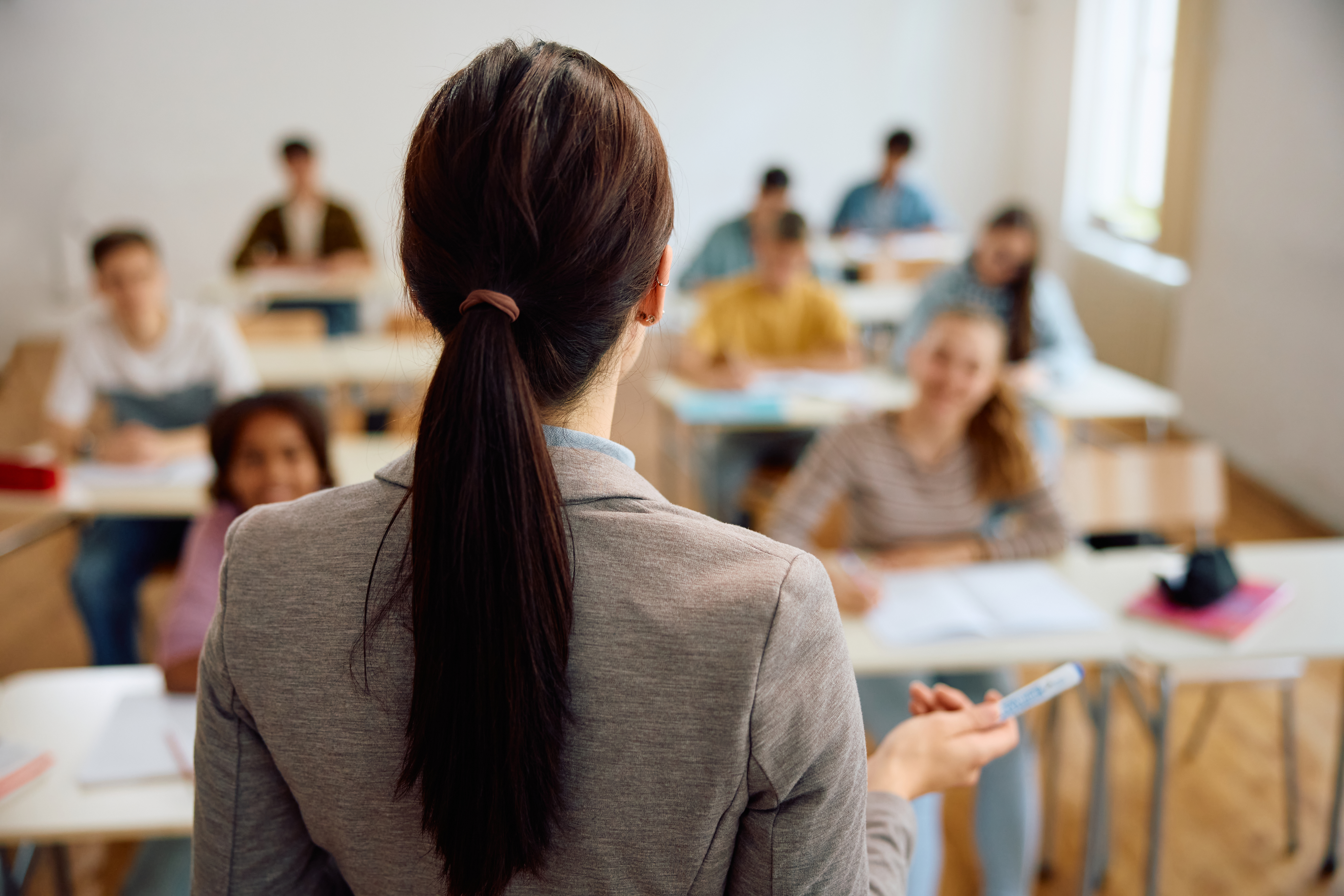 Rear view of professor teaching her students in the classroom at high school.